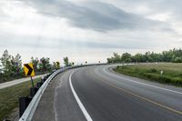 a curved road with signs on the roadsides in front of the sky with clouds and green grass