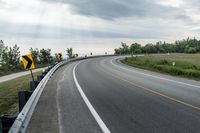 a curved road with signs on the roadsides in front of the sky with clouds and green grass