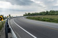 a curved road with signs on the roadsides in front of the sky with clouds and green grass