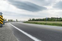 a curved road with signs on the roadsides in front of the sky with clouds and green grass