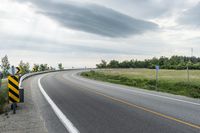 a curved road with signs on the roadsides in front of the sky with clouds and green grass