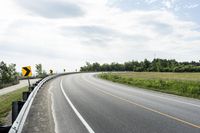 a curved road with signs on the roadsides in front of the sky with clouds and green grass