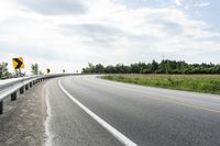 a curved road with signs on the roadsides in front of the sky with clouds and green grass