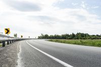 a curved road with signs on the roadsides in front of the sky with clouds and green grass