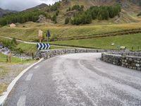 a curved road with a stone foot bridge that goes over it to the next lane