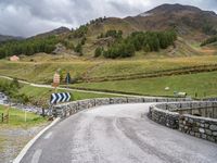 a curved road with a stone foot bridge that goes over it to the next lane