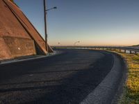 a curved curved road with lights near the ocean and land below the wall at sunset