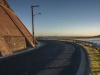 a curved curved road with lights near the ocean and land below the wall at sunset