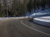 a curved road is shown surrounded by snow on the side of it, with a mountain in the background