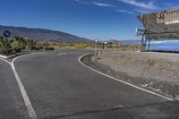 some very neat looking curved road next to a mountain range and sky with some clouds