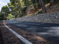 a curved road near some very tall trees on the side of a cliff wall of rock