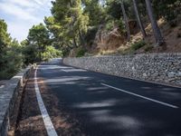 a curved road near some very tall trees on the side of a cliff wall of rock