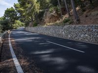 a curved road near some very tall trees on the side of a cliff wall of rock