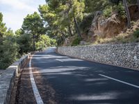 a curved road near some very tall trees on the side of a cliff wall of rock
