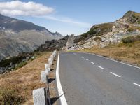 a curved roadway is near the top of a mountain range with the mountain and a grassy area beneath