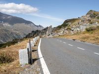 a curved roadway is near the top of a mountain range with the mountain and a grassy area beneath