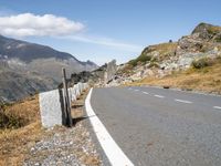 a curved roadway is near the top of a mountain range with the mountain and a grassy area beneath