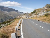 a curved roadway is near the top of a mountain range with the mountain and a grassy area beneath