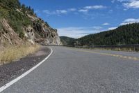 a curved roadway with rocks, grass and trees in the background and blue sky with clouds