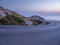 a curved roadway windscreen near the ocean and a hill top lighthouse at dusk - photo of twilight