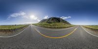 three lane curved roadway with mountains in the background, viewed from the back side on a sunny day