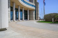 a curved sidewalk leading to an entrance of a building, with columns and bushes on each side of it