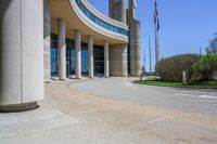 a curved sidewalk leading to an entrance of a building, with columns and bushes on each side of it