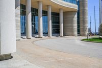 a curved sidewalk leading to an entrance of a building, with columns and bushes on each side of it