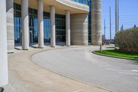 a curved sidewalk leading to an entrance of a building, with columns and bushes on each side of it