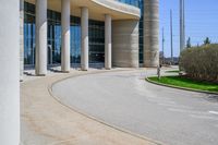 a curved sidewalk leading to an entrance of a building, with columns and bushes on each side of it