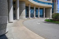 a curved sidewalk leading to an entrance of a building, with columns and bushes on each side of it