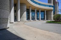 a curved sidewalk leading to an entrance of a building, with columns and bushes on each side of it