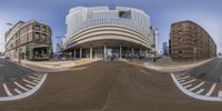 the panoramic view shows how a very large building looks like, while buildings stand around a curved street corner