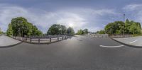 a view of a curved street as it travels past a fence and some trees that are in the distance