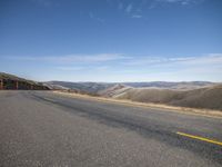 a man riding a skateboard down a road surrounded by hills and dry grass on a sunny day