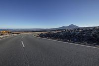 a curving highway with mountain and blue sky in background - some rocks are visible along the street