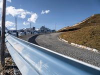 a curving, curved hill road with mountains behind it on a clear day with blue sky