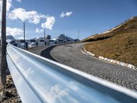 a curving, curved hill road with mountains behind it on a clear day with blue sky