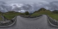 the fisheye view of a curve on a road with mountains in the background and a small red umbrella on top of the curb