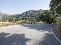 the empty road is in front of mountains, trees and rocks, with a white line going through it