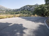 the empty road is in front of mountains, trees and rocks, with a white line going through it