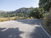 the empty road is in front of mountains, trees and rocks, with a white line going through it