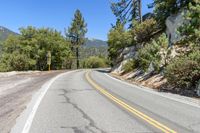 a road curves down the side of a rocky mountain with some trees on the far side