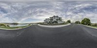 a fish - eye shot shows an empty, curving road leading to a two story house with water view in the background