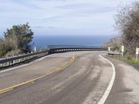 a bike rider leans on the road towards the ocean shore as he passes a curvy curve