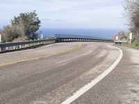 a bike rider leans on the road towards the ocean shore as he passes a curvy curve