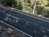 a man riding a bike down a winding road surrounded by trees on a cliff wall