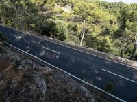 a man riding a bike down a winding road surrounded by trees on a cliff wall