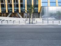 a person riding a bike down a street past a building with tall windows and silver fencing