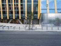 a person riding a bike down a street past a building with tall windows and silver fencing